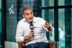 الإعلامي المصري باسم يوسف جالساً على كرسي ويحمل مايكروفون بيده وهو يتحدث.