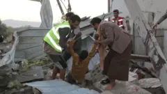 Йеменские спасатели вытаскивают раненого мужчину из-под обломков здания, пострадавшего, по утверждению хуситов, в результате ударов США в провинции Саада, 28 апреля 2025 года.