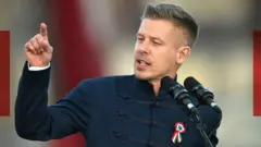 Peter Magyar gesticula em um pódio. Ele veste um paletó azul de gola alta com brocado na frente e tem uma roseta presa ao peito.