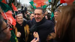 Homem de óculos no meio de várias pessoas com bandeiras de Portugal