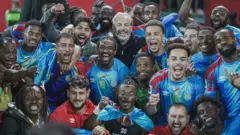 Abakinnyi ba DR Congo bari kumwe n'umutoza Sébastien Desabre (wambaye umupira w'umukara inyumna hagati) bishimira intsinzi mu ijoro ryo ku cyumweru