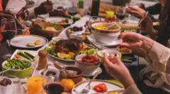 Mesa repleta de alimentos diversos com pessoas fazendo sua refeição