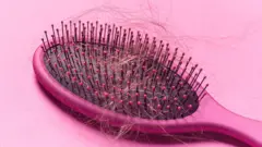 Escova com fios de cabelo soltos sobre um fundo rosa