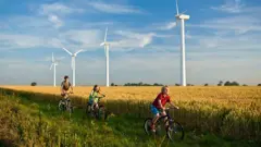Kids cycling past wind turbines in the country