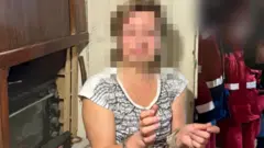 Жінка стоїть в кімнаті й жестикулює руками 