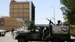 Personal militar vigilan los restos del centro comercial incendiado.