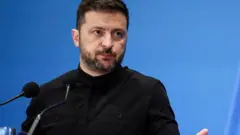 Perezida wa Ukraine Volodymyr Zelenskiy akoze ikimenyetso n'ikiganza mu kiganiro n'abanyamakuru
