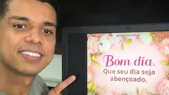 O empresário Ricardo Araújo sorri em frente a uma tela de computador que mostra uma mensagem de bom dia