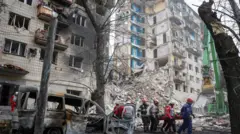 Imagem de socorristas carregando um corpo diante de um prédio residencial destruído, em Kiev, durante um ataque russo