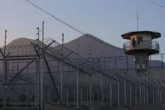 Un funcionario de prisiones hace guardia en la torre de vigilancia con el volcán San Vicente al fondo en el centro penitenciario de máxima seguridad CECOT (Centro de Internamiento Obligatorio para Terroristas) el 4 de abril de 2025 en Tecoluca, San Vicente, El Salvador.