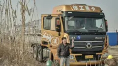 Un homme prend un selfie devant son camion, devant lequel sont disposés des équipements et du matériel de camionnage.