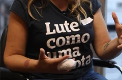 Michelle Bernardes fotografada do pescoço para baixo, com o dedo enfaixado após incidente que resultou na amputação parcial do membro. Ela veste uma camiseta preta onde se lê em letras brancas "Lute como uma garota"