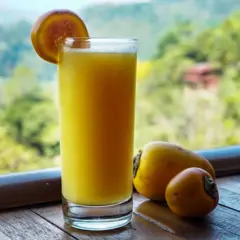 Copo com um suco alaranjado ao lado de duas frutas