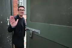 Vestindo terno preto e camiseta, Andy Burnham acena em despedida ao deixar o People's History Museum, em Manchester, Reino Unido, após proferir um discurso, em 29 de junho de 2026.