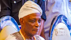 Rashidi Ladoja sitting looking straight, e wear cap and beads for neck