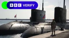 Sous-marins russes à quai à Tartous en 2019. Un soldat armé se tient à côté des navires sur un quai. 