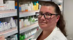 A farmacêutica Yasmine Lindberg, com remédios ao fundo, em uma prateleira