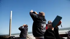 People photograph a suspected Chinese spy balloon as it floats off the coast in Surfside Beach, South Carolina, U.S. February 4, 2023.