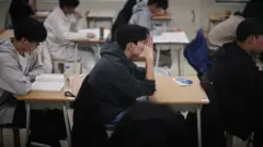 試験会場で受験生たちが着席し、大学修学能力試験の開始を待っている。顔に手をやったり、参考書らしきものを読んだりしている