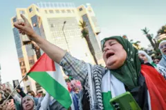 سيدة محجبة تتوشح بالعلم الفلسطيني والكوفية الفلسطينية وترفع يدها في انفعال خلال تجمع قافلة الصمود في تونس 