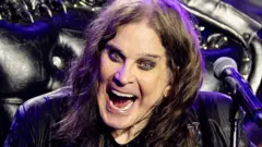 Ozzy Osbourne on stage with his arms outstretched and a big open-mouthed grin