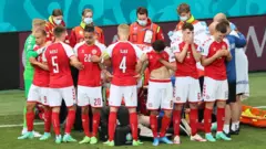 Los jugadores de Dinamarca forman un círculo para proteger a su compañero Christian Eriksen mientras recibe asistencia médica durante el partido del Grupo B de la Eurocopa 2020 entre Dinamarca y Finlandia en 2021.