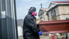 Trabajadores de salud cargando un ataúd de un fallecido de covid-19.