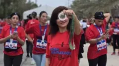 Mulheres iranianas vestem uma camisa vermelha com a logo da maratona. Uma delas mostra uma medalha