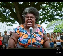 Avatar de inteligência artificial representa uma mulher idosa negra que grita em um microfone, com público ao fundo