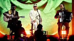 Jotapê tocando violão, João Gomes cantando e Mestrinho tocando acordeão; eles estão sentados em palco