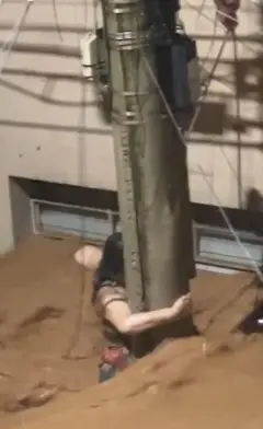 Mulher agarrada em poste no meio de enchente