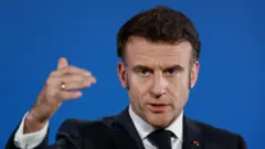 O presidente francês Emmanuel Macron, com um ar severo em um terno azul-marinho, fala durante uma coletiva de imprensa após uma cúpula de líderes europeus para discutir a Ucrânia e a defesa europeia