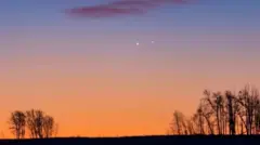 Foto colorida mostra dois pontos brilhantes no céu com cores alaranjadas do por do sol