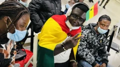 Man put Ghana flag for im head wit headphone, anoda man dey beside am wit nose mask
