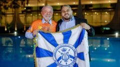 Lula com blusa laranja ao lado de Wallace Palhares. Ambos seguram na frente a bandeira azul e branca da Acadêmicos de Niterói. Ao fundo, a imagem mostra a piscina e o Palácio da Alvorada desfocados.