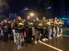 Млади људи држе букете белих ружа на киши током ноћи, у колони