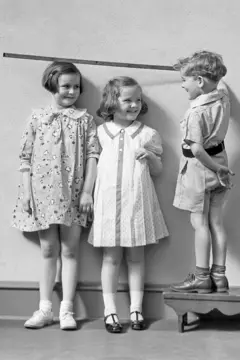 Três crianças brincam com uma régua junto a uma parede