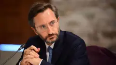 Fahrettin Altun mikrofon başında, bir başka kişiyi dinliyor