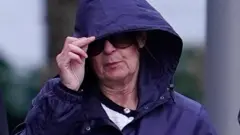 Joanne Sharkey, vestindo um casaco azul com o capuz puxado sobre o cabelo e grandes óculos de sol, do lado de fora do tribunal em Liverpool