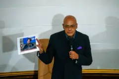 O presidente da Assembleia Nacional da Venezuela, Jorge Rodríguez, veste terno escuro e segura uma fotografia da primeira-ministra de Trinidad e Tobago.