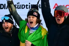 O brasileiro Lucas Pinheiro Braathen (C), segundo colocado, comemora com sua equipe no pódio após competir no slalom gigante masculino da Copa do Mundo de Esqui Alpino da FIS 2025-2026, em Alta Badia, norte da Itália, em 21 de dezembro de 2025.