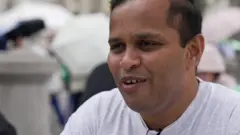 Pai de Bodhana dando entrevista. Ele usa uma camisa branca