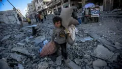 Palestinian children collect usable belongings from the rubble after the Israeli strike on Abu Hasira Street in Gaza City, Gaza, on 30 September 30 2025. Several buildings are completely destroyed in the background.