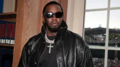 Sean "Diddy" Combs wear black sunglasses, black leather jacket, chain with a cross and a black T-shirt. 