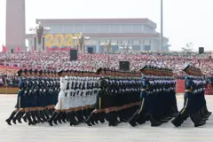 Soldados con uniforme ceremonial marchan frente a un podio abarrotado.