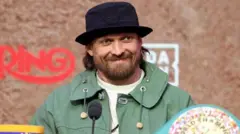 Oleksandr Usyk smiles and is wearing a black bucket hat and green coat