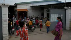 Trabalhadores da indústria do vestuário chegando ao trabalho em uma fábrica em Phnom Penh, no Camboja, muitos deles de motocicleta