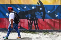 Homem passa por um mural com uma bomba de extração de petróleo, com a bandeira da Venezuela ao fundo
