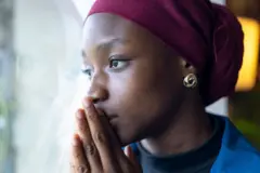 Jeune femme en foulard regardant par la fenêtre, les mains couvrant sa bouche 