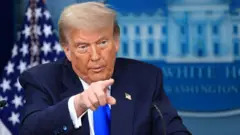 Trump on black suit, e dey point im finger